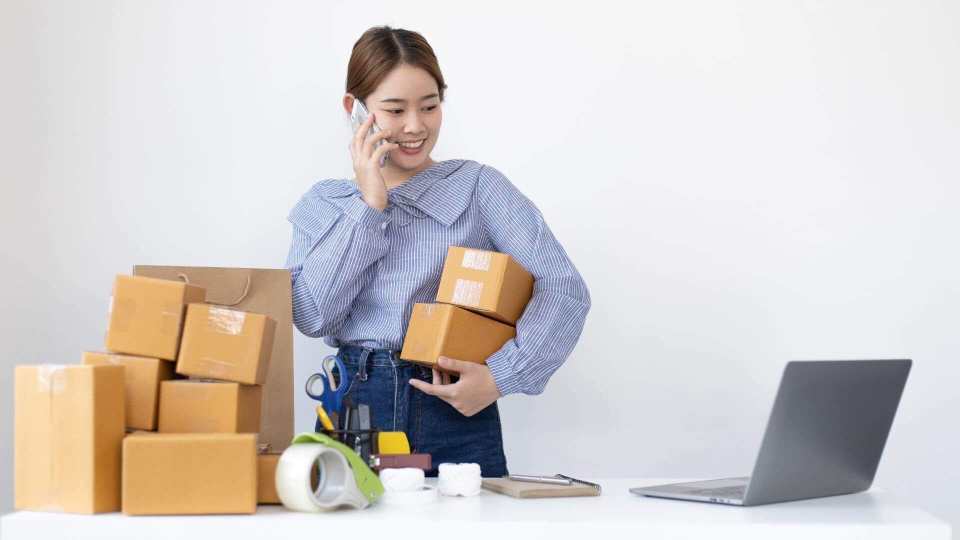 Seller on the phone beside a stack of parcels and a laptop