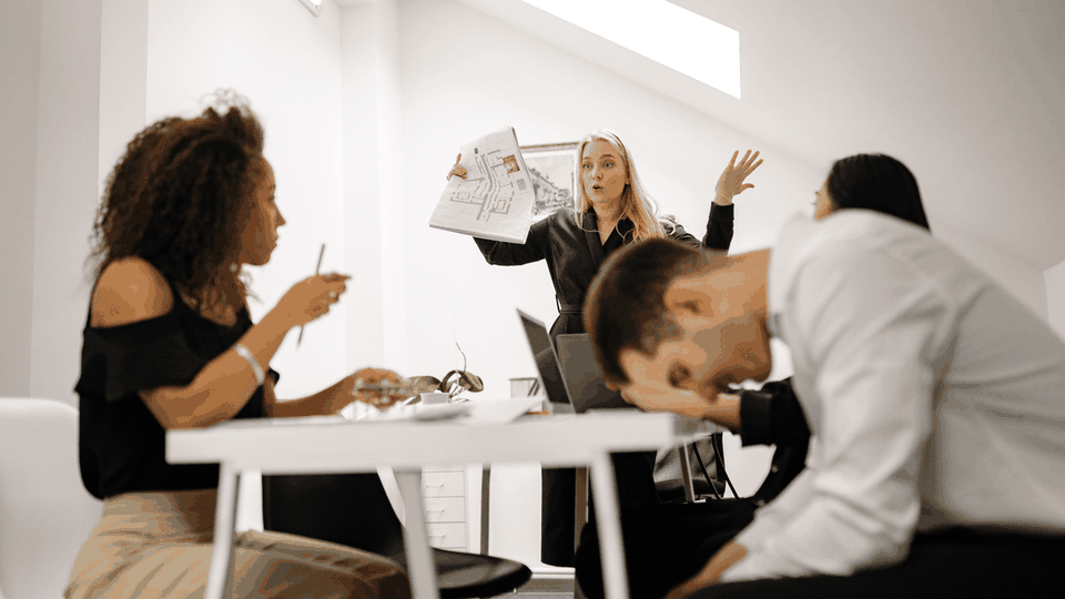 Team at a meeting table looking overwhelmed, one slumped over the desk