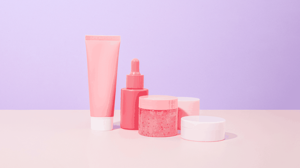 Skincare tube, serum dropper and open cream jars on a lilac background