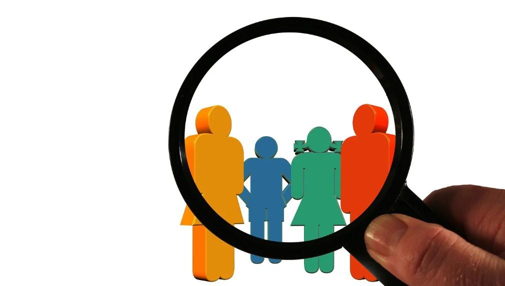 Magnifying glass held over a row of colourful paper cut-out figures