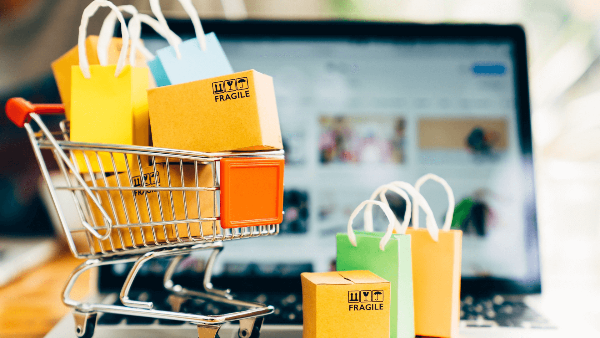 Miniature shopping trolley holding parcels and gift bags in front of a laptop