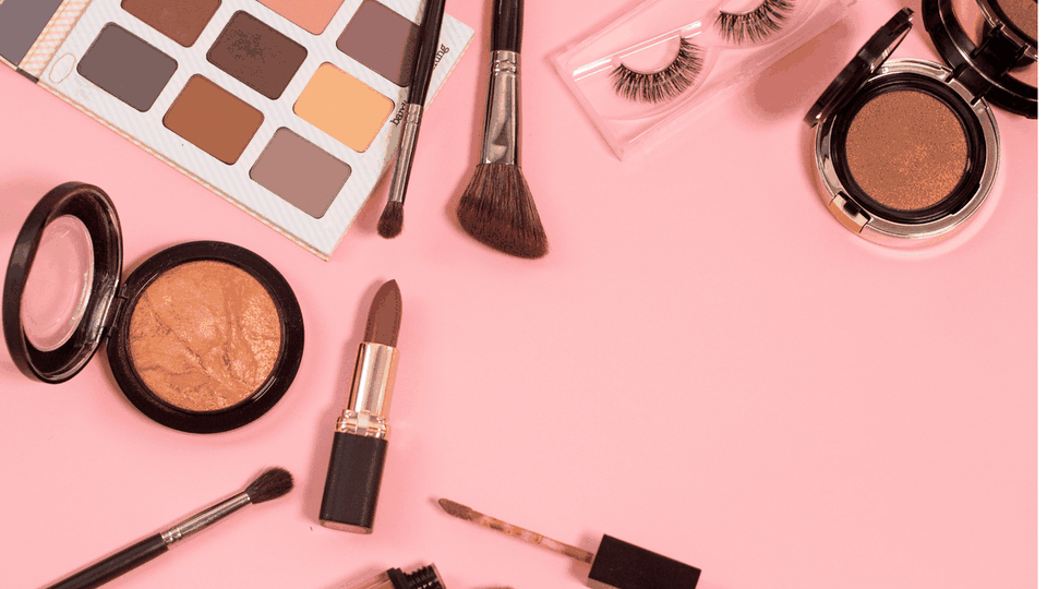 Eyeshadow palette, makeup brushes, lipstick and false lashes on a pink background