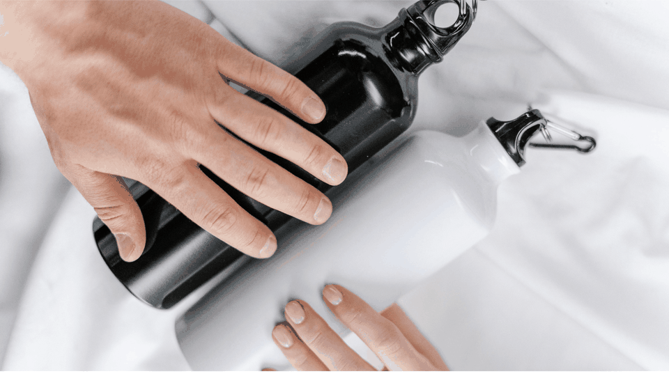 Hands holding a black insulated water bottle beside a white one